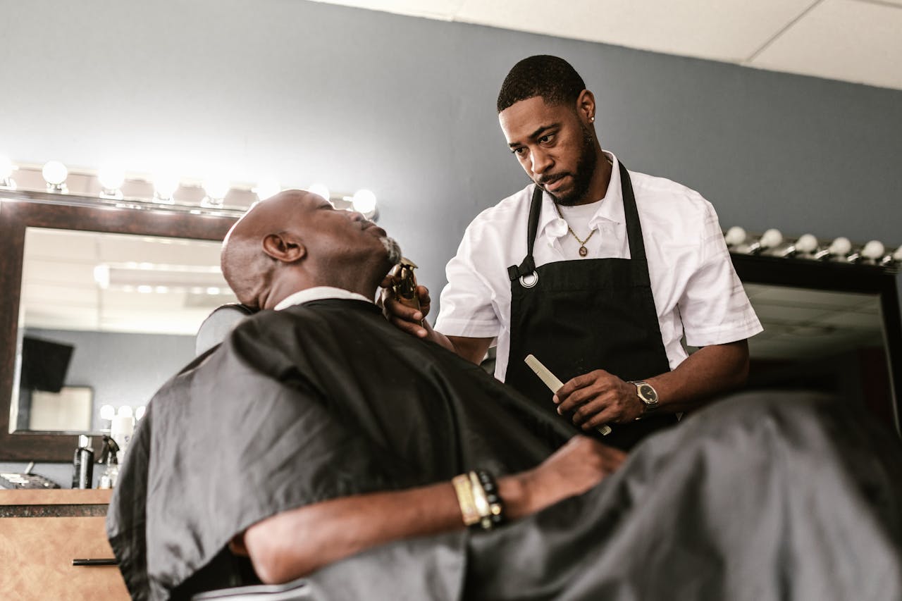 A barber carefully trims a customer's beard in a modern salon setting.