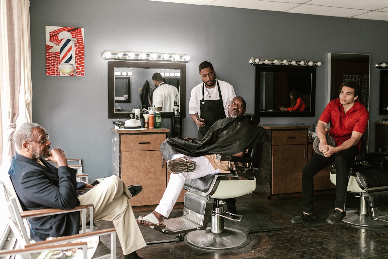 Home A stylish barber shop with clients and a barber in a relaxed setting, showcasing a classic grooming experience.